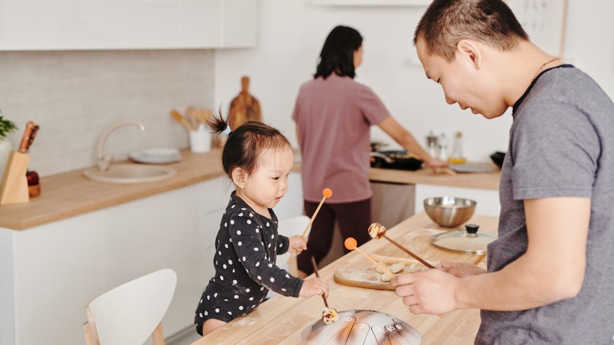 Father and child enjoy bonding over music in a cozy modern kitchen setting.