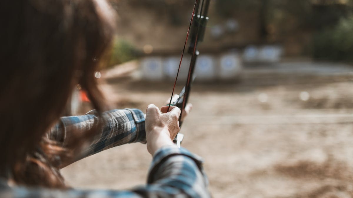 A woman aims a recurve bow at targets during outdoor archery practice.